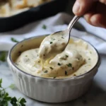 Smooth and creamy Alfredo sauce dripping from a spoon into a white bowl.